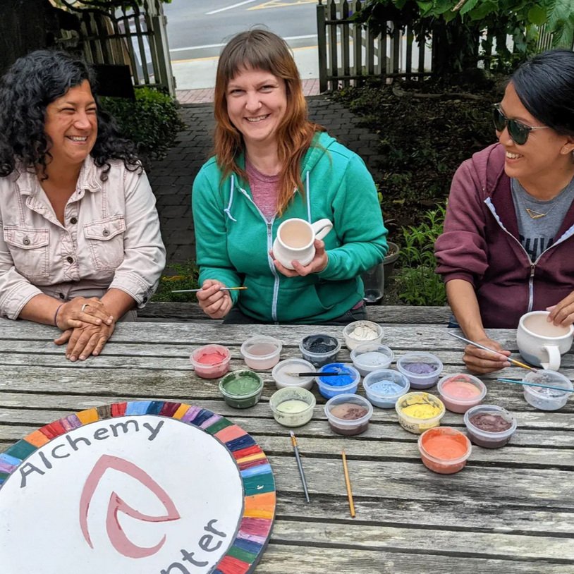 Friends painting pottery at an outdoor table