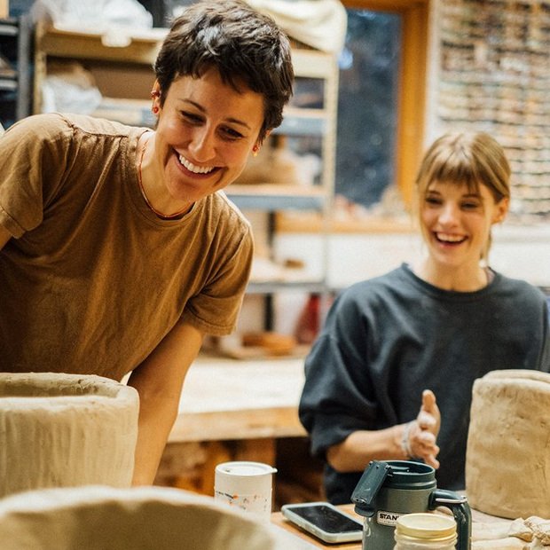 Two people smiling as they handbuild in clay