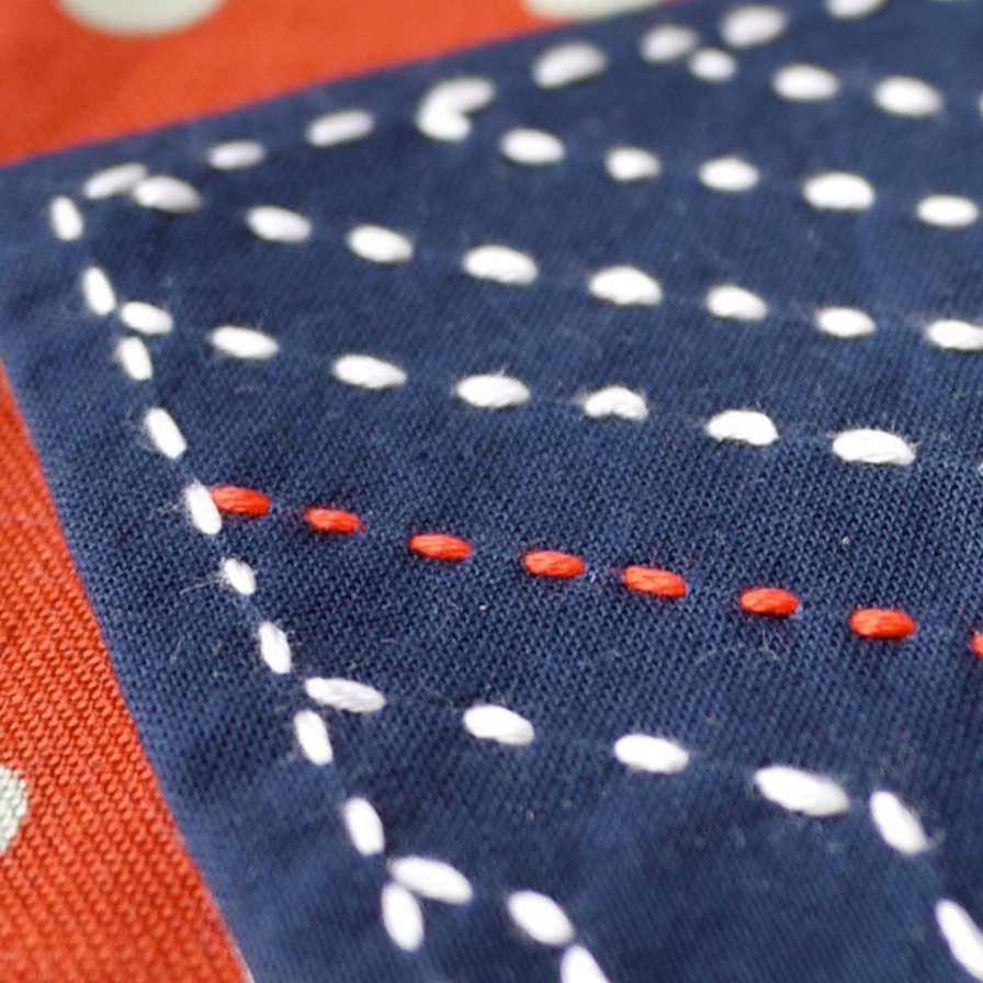 Sashiko running stitches in white and orange on indigo cloth
