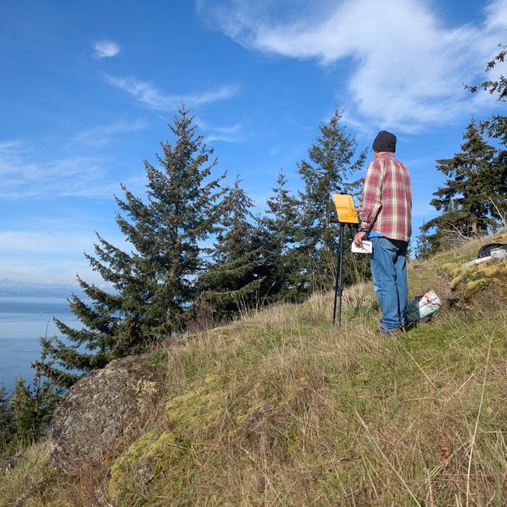 A painter at an easel on a hillside above the water